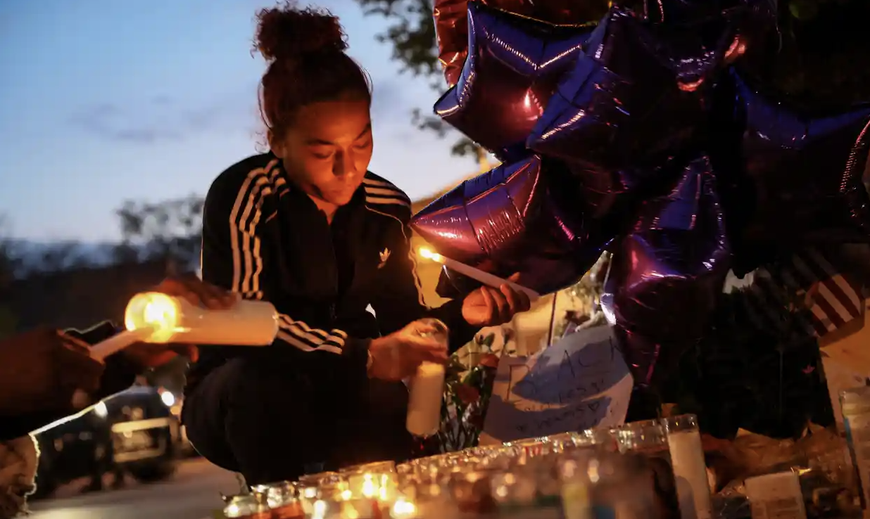 Young Black woman lighting candles next to balloons in the evening outside. Photograph: Brendan McDermid/Reuters